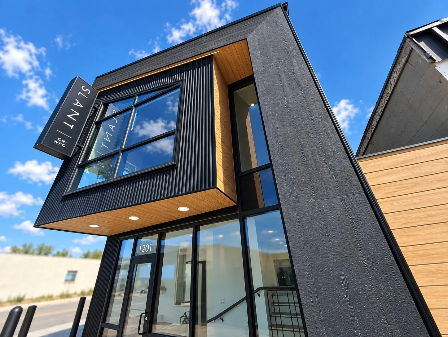 SLANT from the street, looking up at the black cladding, the wood soffit and the tall corner windows
