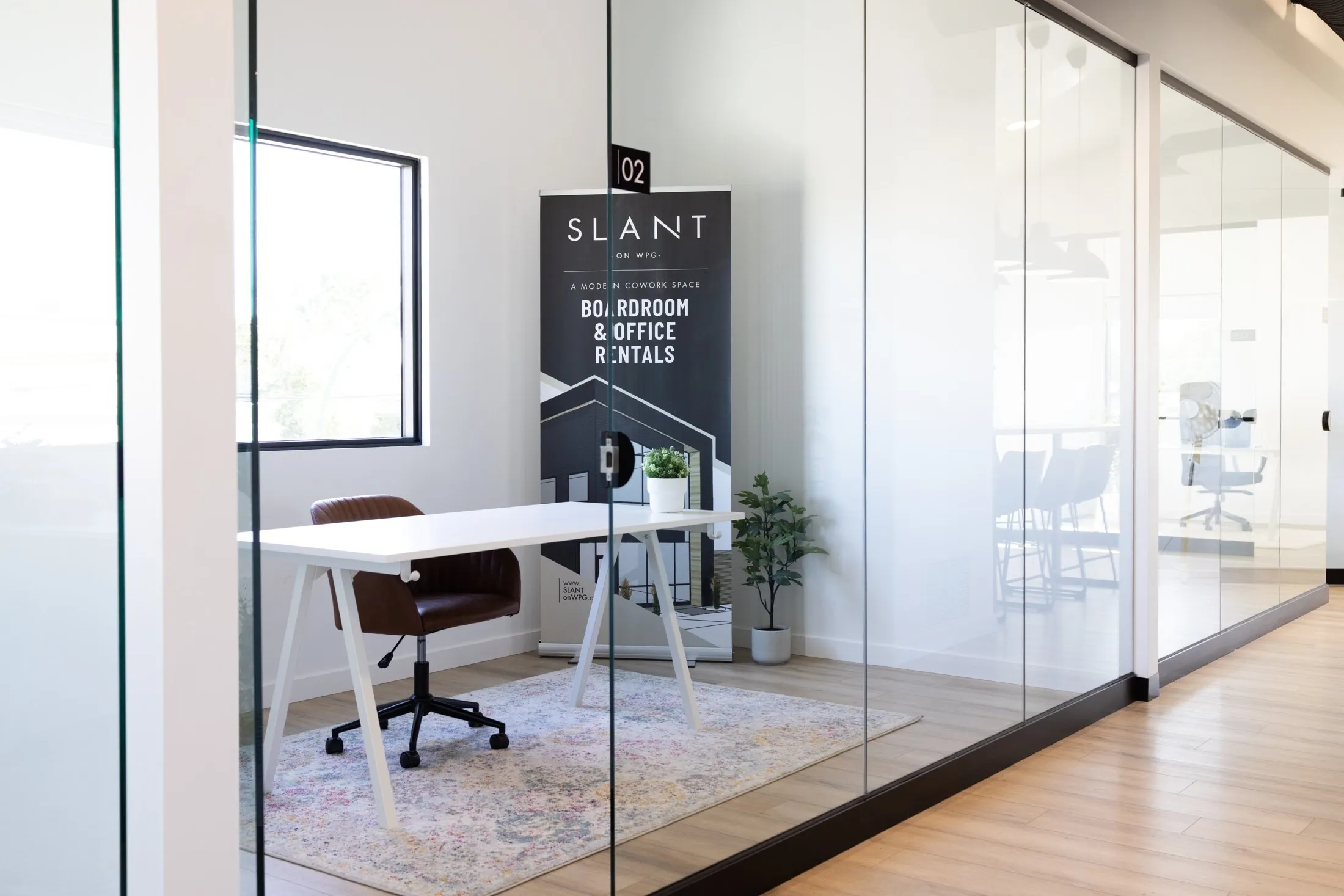 Office 2 seen through its glass wall, a white desk and leather chair on a patterned rug